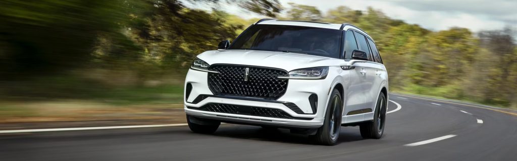 White luxury SUV driving on a winding road, with trees and greenery blurred in the background.