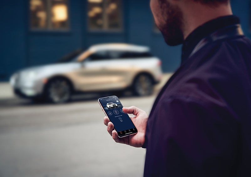 A person is shown interacting with a smartphone to connect to a Lincoln vehicle across the street. | West Point Lincoln in Houston TX