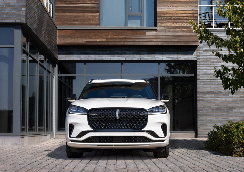 A white 2025 Lincoln Aviator® SUV is shown parked outside a modern building with gray brick and wood accents. | West Point Lincoln in Houston TX