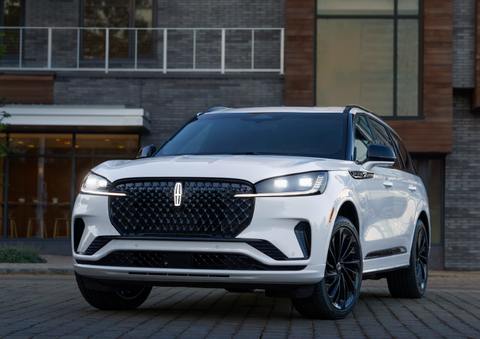 A white 2025 Lincoln Aviator® SUV is shown parked outside a modern building with gray brick and wood accents. | West Point Lincoln in Houston TX