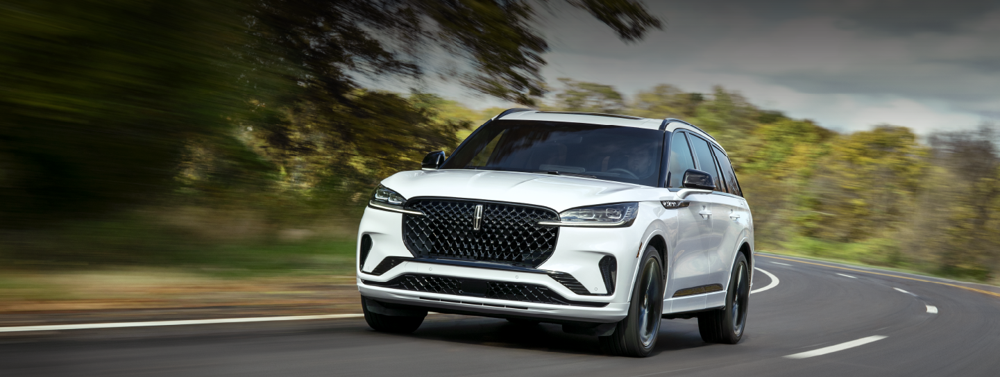 A white 2025 Lincoln Aviator® SUV is being driven down a road lined with trees. | West Point Lincoln in Houston TX