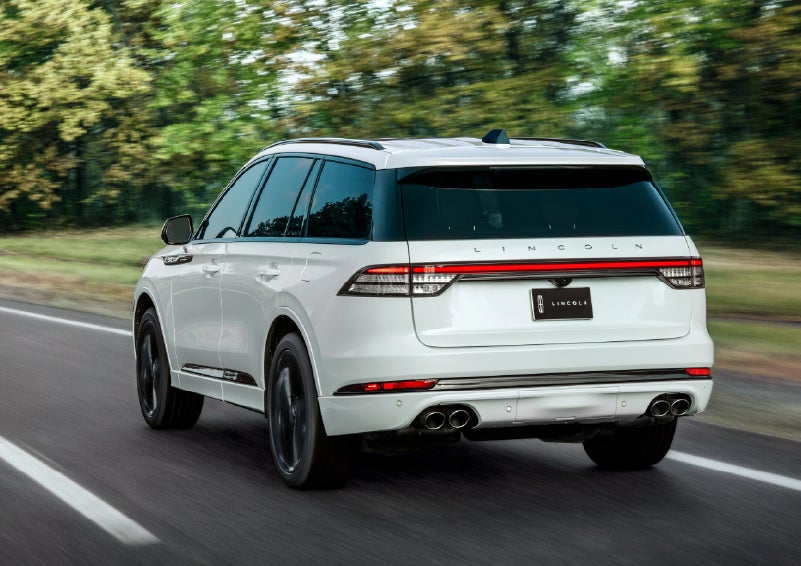 A white 2026 Lincoln Aviator® SUV is being driven away down a road lined with colorful trees. | West Point Lincoln in Houston TX