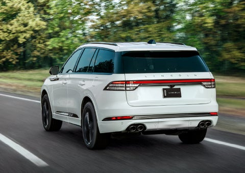 A white 2026 Lincoln Aviator® SUV is being driven away down a road lined with colorful trees. | West Point Lincoln in Houston TX