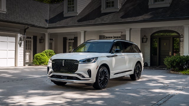 A white 2026 Lincoln Aviator® SUV is parked in the driveway of a luxury home. | West Point Lincoln in Houston TX