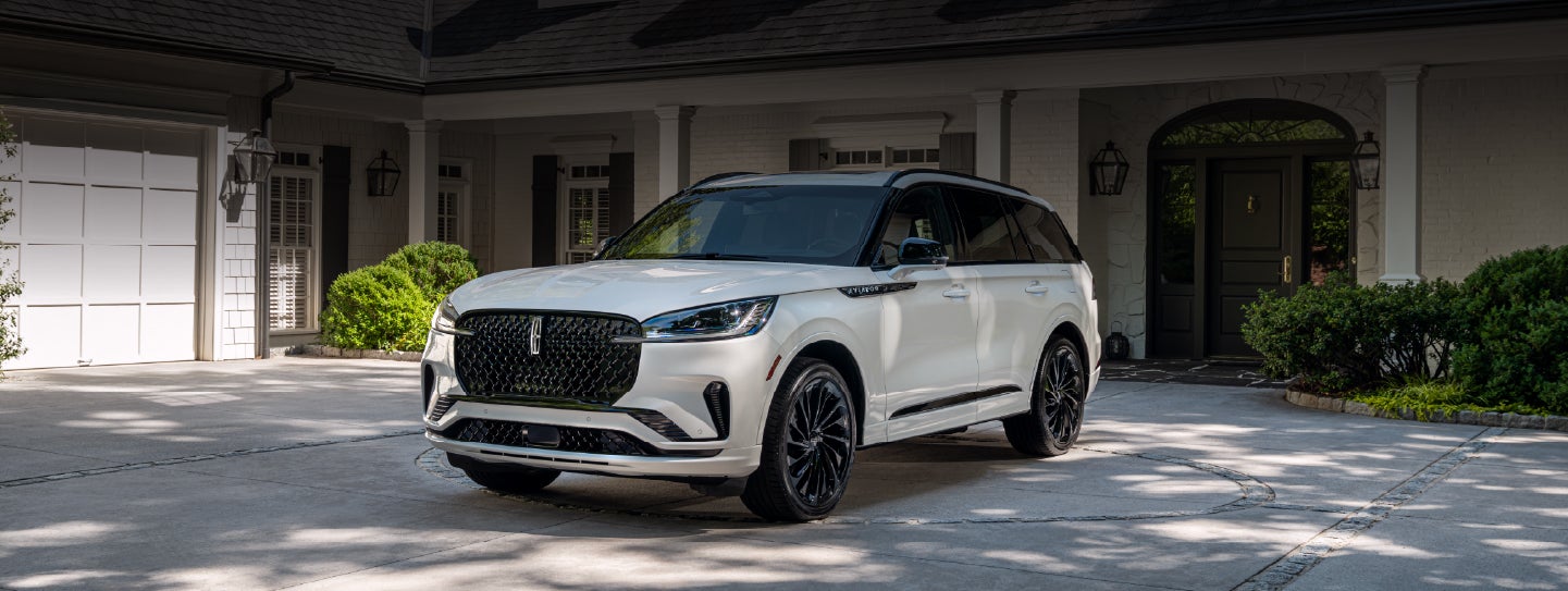 A white 2026 Lincoln Aviator® SUV is parked in the driveway of a luxury home. | West Point Lincoln in Houston TX