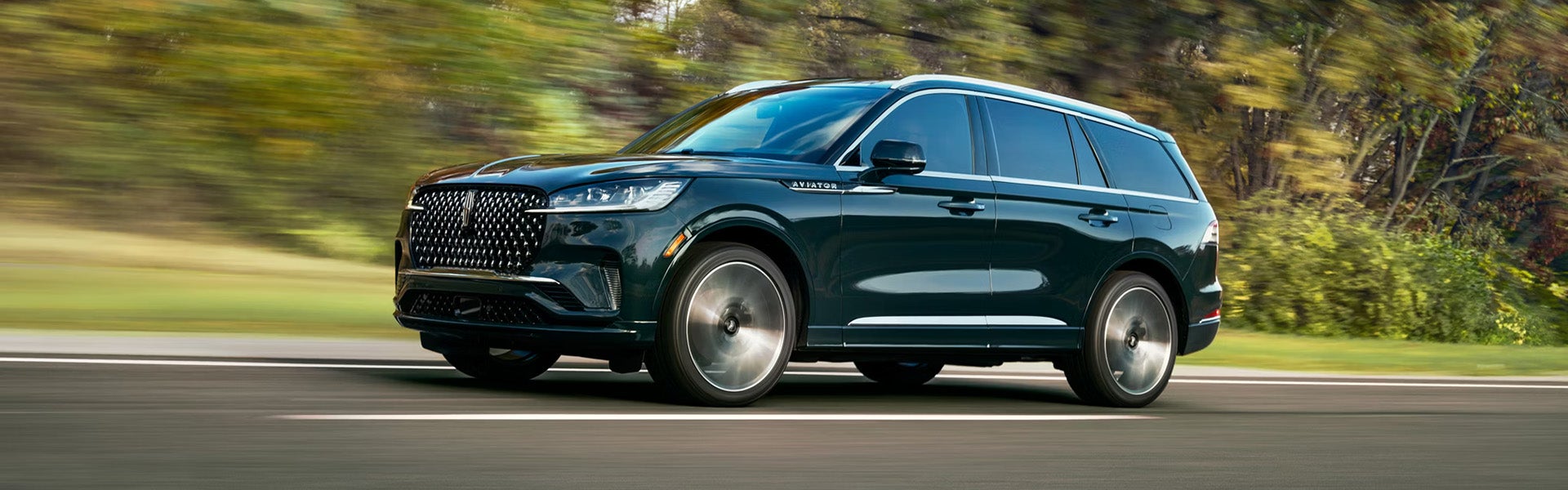 Dark green Lincoln Aviator SUV driving on a road with a blurred forest background.