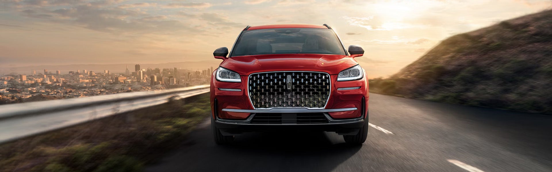 Red Lincoln SUV driving on a winding road with a city skyline and sunset background