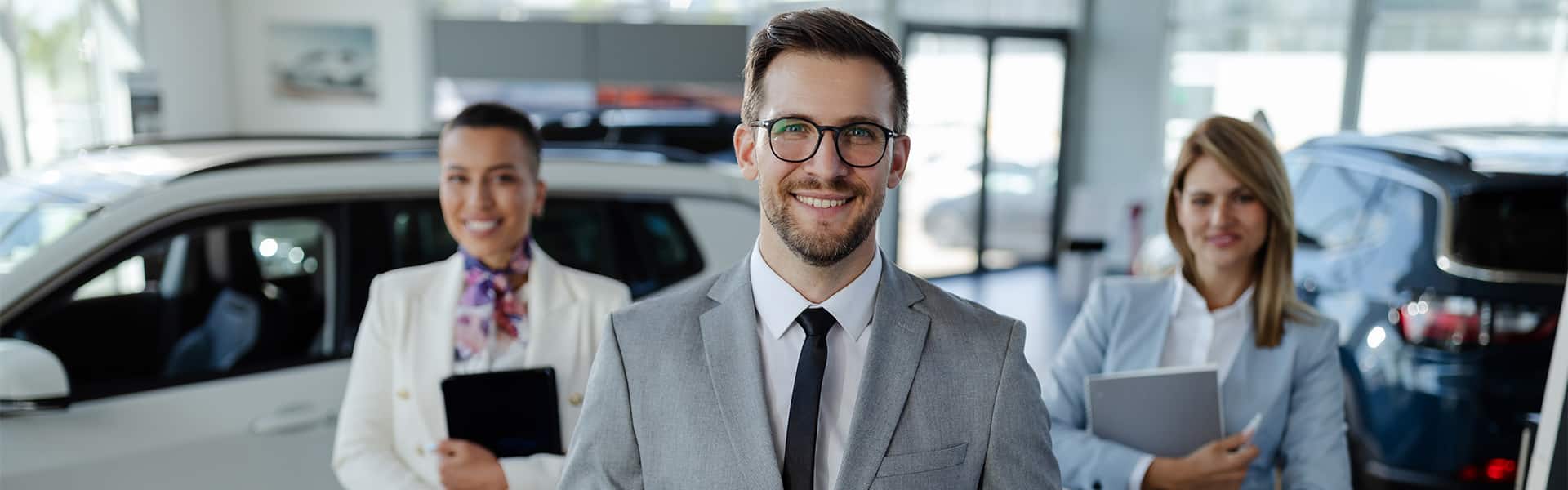 Car dealership team members assisting customers in a showroom with vehicles in the background, representing vehicle ownership and customer support.